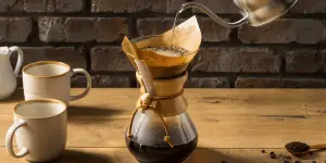 At home pour over coffee maker on a wooden table with two light brown coffee cups on the left side of the pour over coffee maker