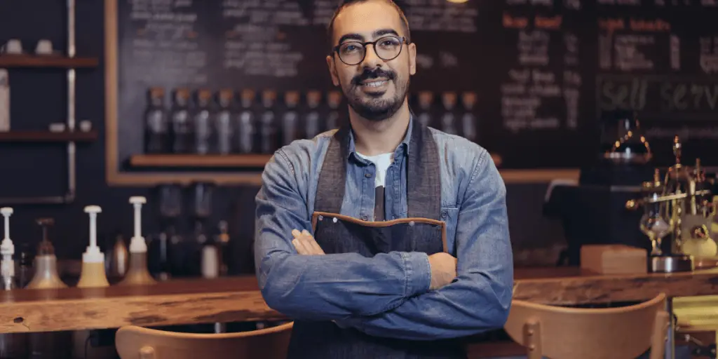Barista standing with his arms crossed and big smile.