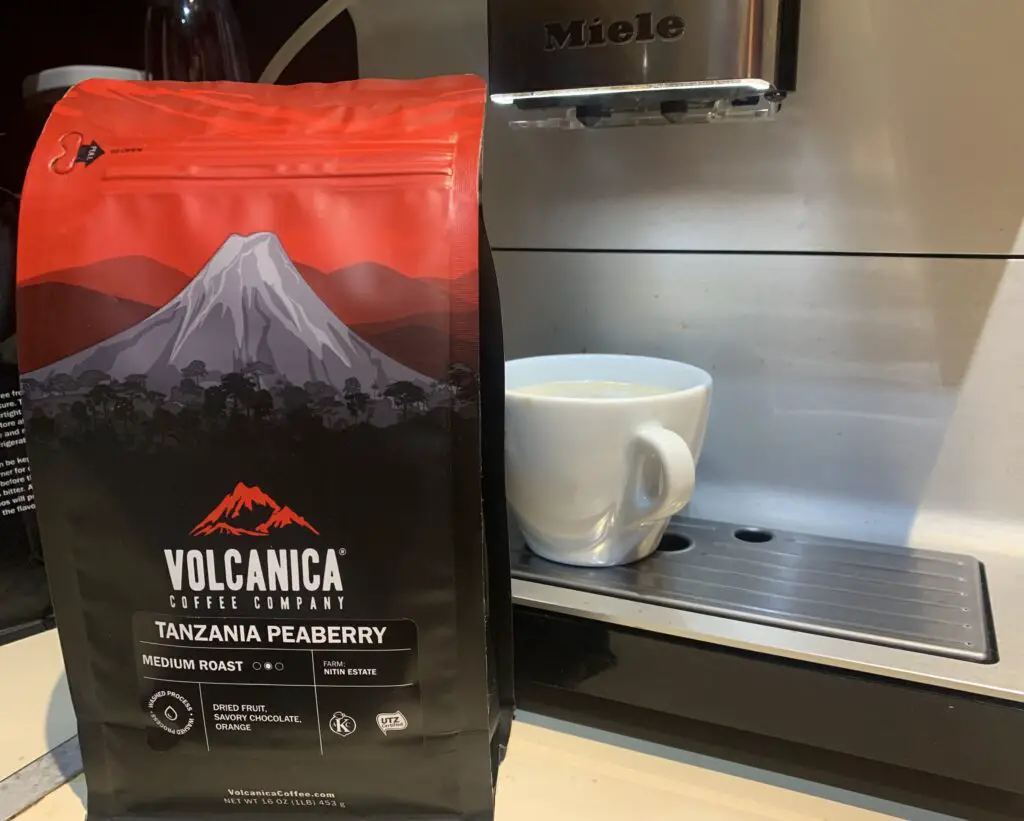 Bag of Tanzania Peaberry coffee beans by Volcanica in front of bean to cup machine