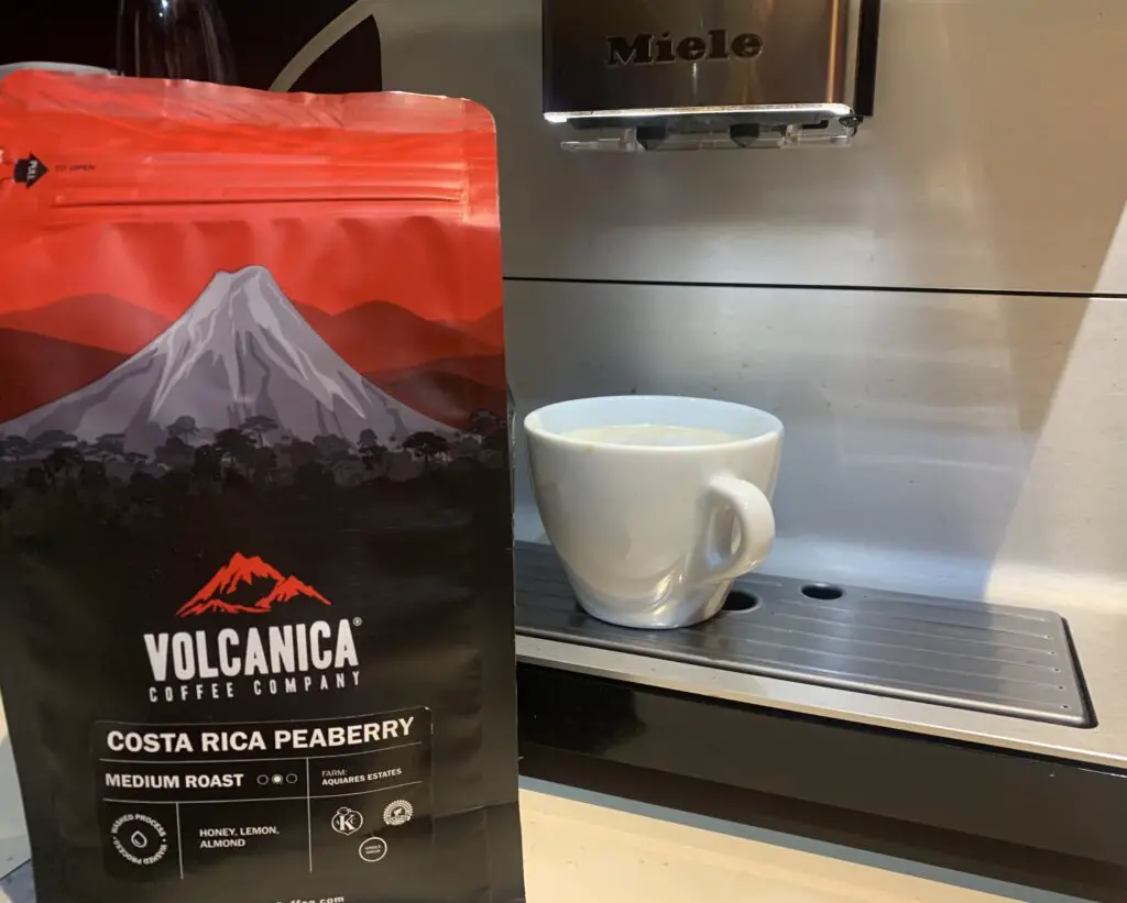 Bag of Costa Rica Peaberry coffee beans by Volcanica in front of bean to cup machine