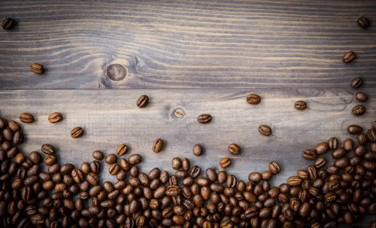 A large number of peaberry coffee beans on a wooden counter.