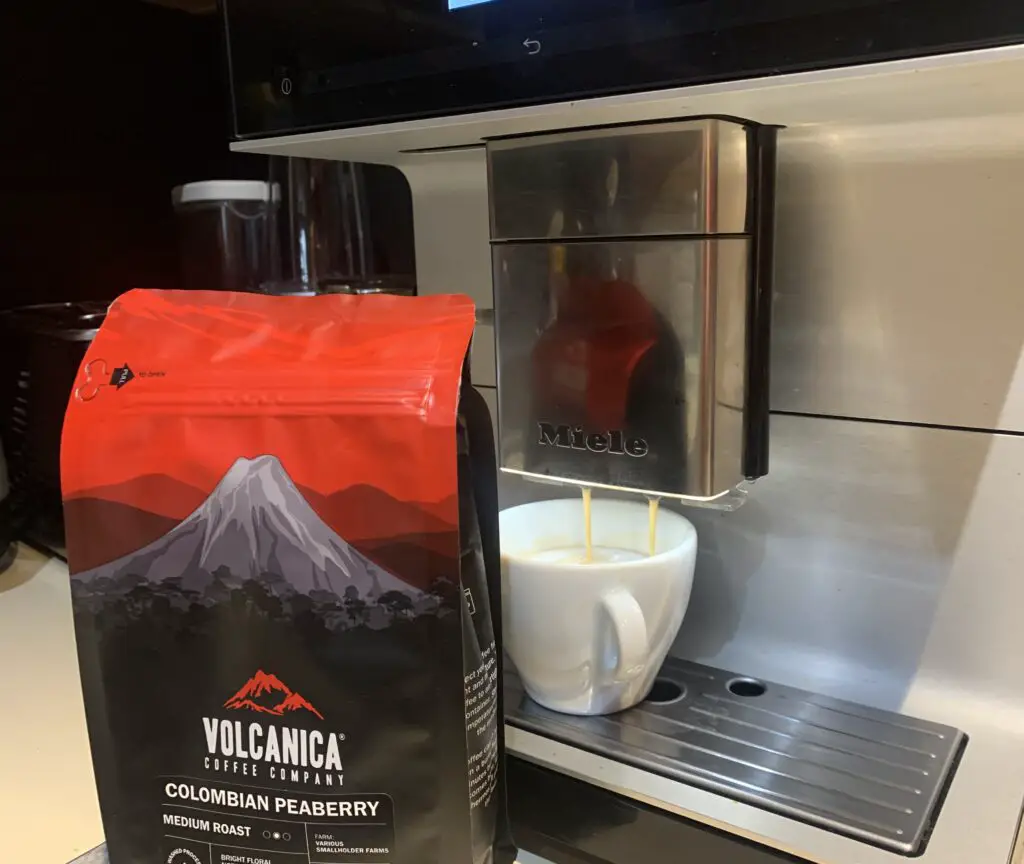Bag of Columbian Peaberry coffee beans by Volcanica in front of bean to cup machine