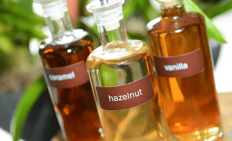 Up close view of 3 small clear bottles filled with hazelnut, vanilla and caramel coffee oils