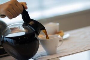 A cup of coffee being poured from a pot of coffee into a white cup.