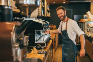 Male barista smiling and making coffee behind a bar counter.