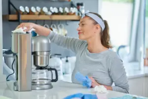 Woman cleaning a coffee maker with a coffee pot using a soft towel.
