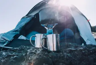 Make coffee while camping on a hot fire outside a blue tent.