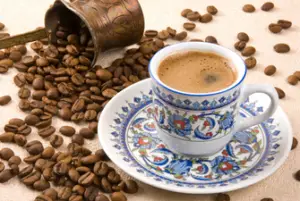 A cup of Turkish coffee surrounded by Kona coffee beans that spilled on the counter.