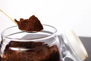 A jar containing coffee grounds that has been opened showing fresh coffee grounds on a spoon.
