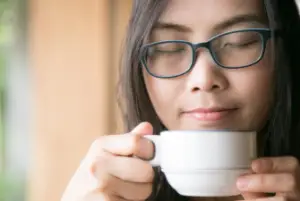 A woman smelling her coffee and asking the question why does coffee smell like cigarettes?