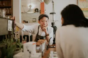 An overworked barista leaning on the coffee counter thinking: is being a barista hard?