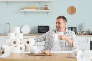 Man smiling while holding coffee cup next to a large number of toilet rolls because decaf coffee make you poop.